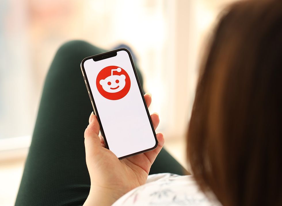 A woman holding a phone with the Reddit logo on the home screen