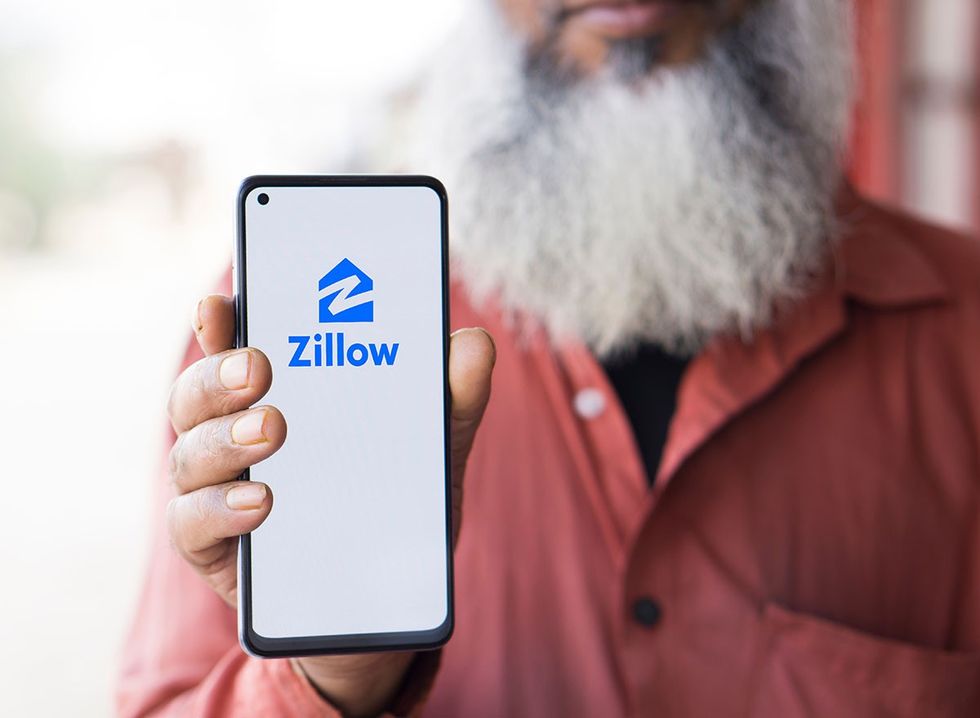 A man holding a cell phone with the Zillow app launched