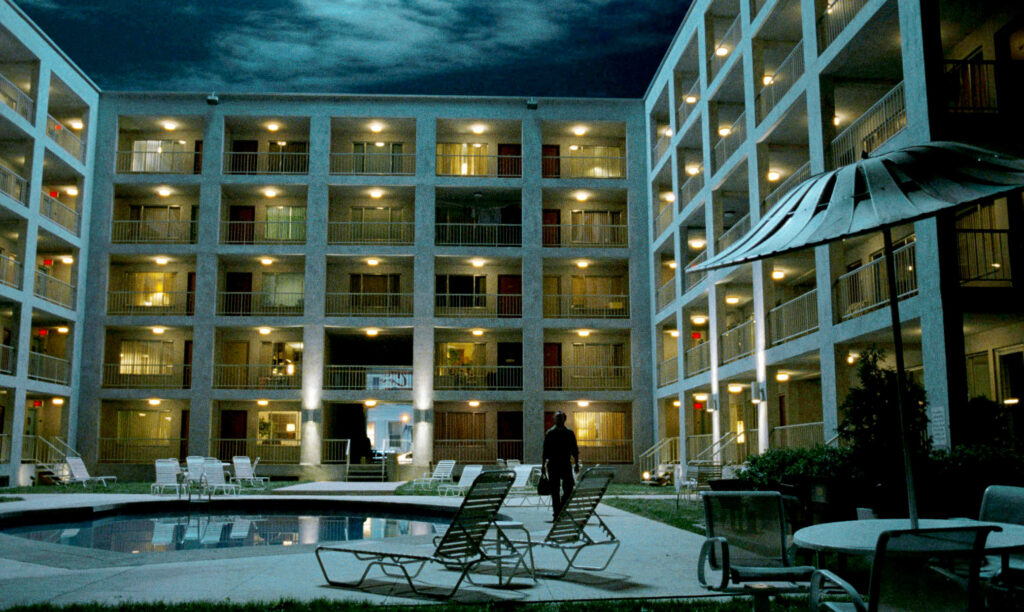 A man walks by the pool of an apartment complex, as the lights beam on in the hallways, in Lady in the Water