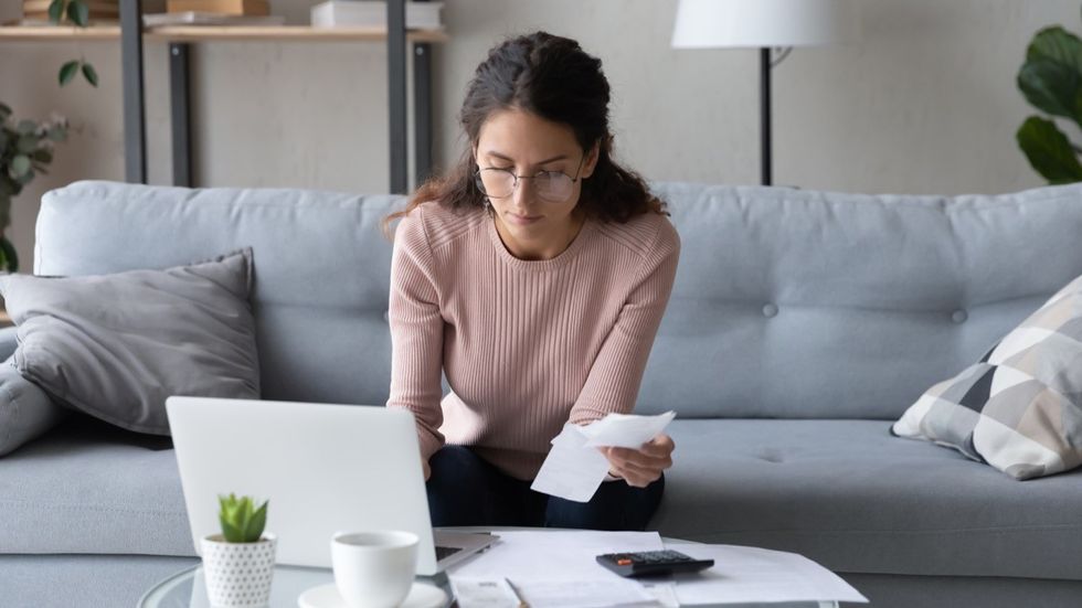 Serious young woman in glasses sit in living room pay bills taxes on laptop online