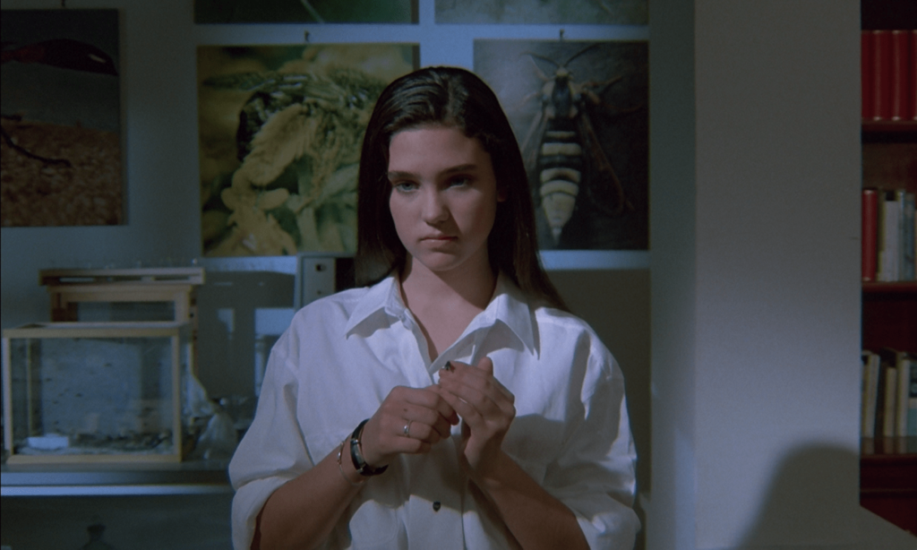 Jennifer Connelly standing in front of a wall decorated with posters of insects in Phenomena.