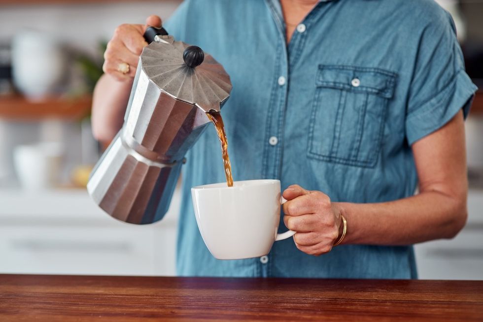 closeup of a woman in a denim shirt pouring coffee from a small metal coffee pot