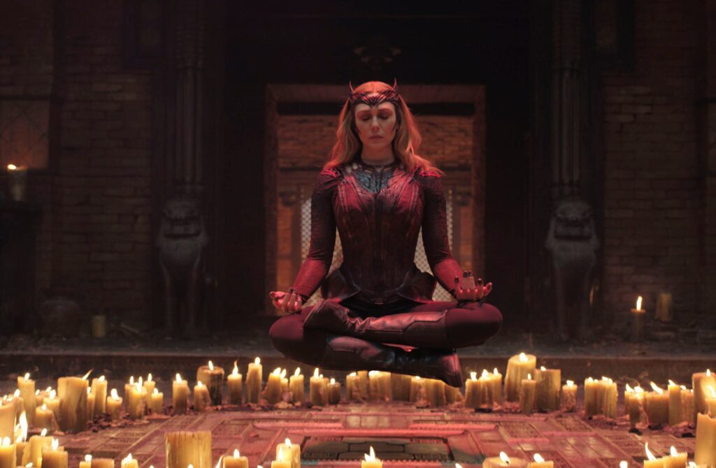 Elizabeth Olsen as Wanda Maximoff floats in the air in lotus position, eyes closed, above a circle of candles in Doctor Strange in the Multiverse of Madness.