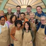 A group of people in tan aprons standing in three rows with their arms around their shoulders.