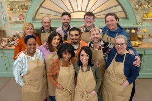 A group of people in tan aprons standing in three rows with their arms around their shoulders.