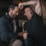 Ryan Reynolds and Hugh Jackman sitting on a couch acting out a fight between Deadpool and Wolverine