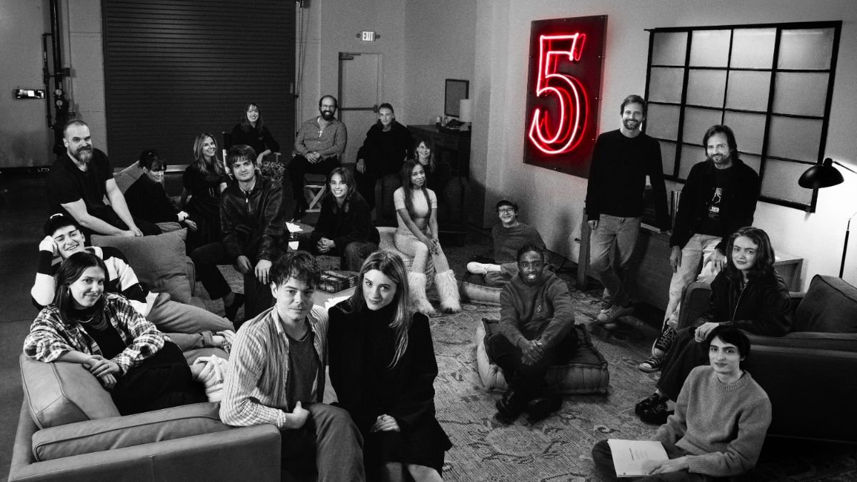 cast of stranger things 5 together in a black and white photo with a glowing number five on the wall 