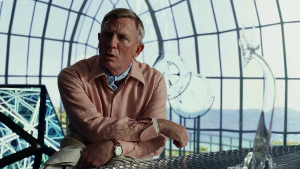 Daniel Craig wears a light pink jacket and is sitting in a glass dome.