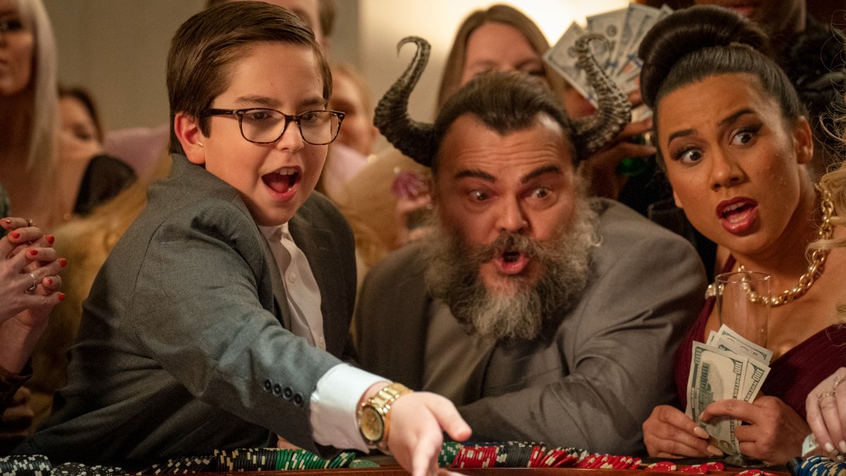 A little boy in a suit gambling with a man who has antlers and a women looking at the gambling table surprised.