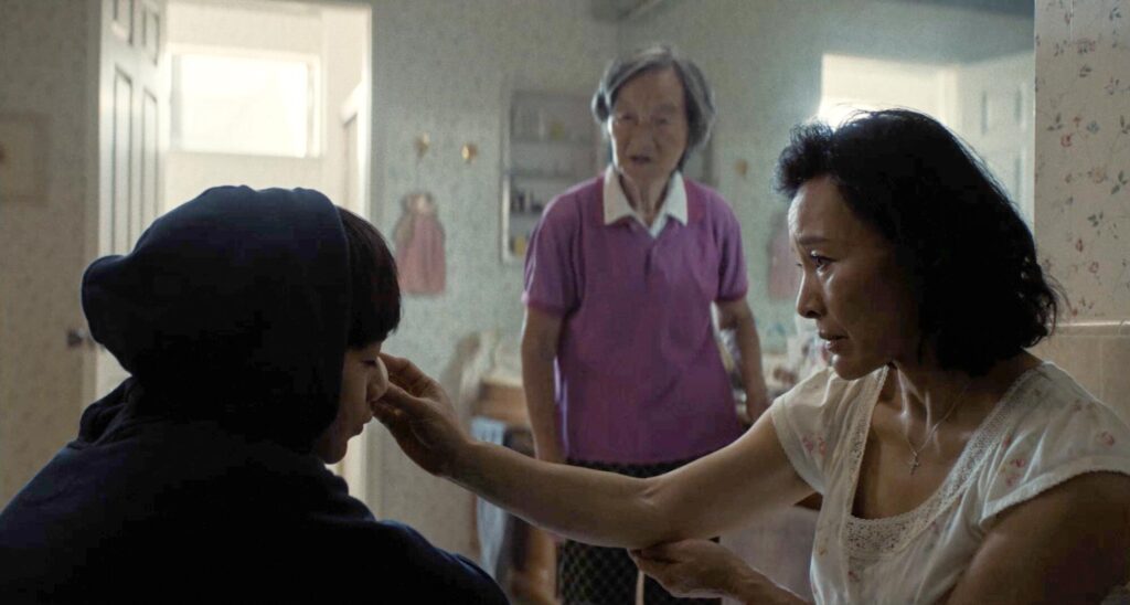 A woman holds her hand to a child's face, as an older woman watches.