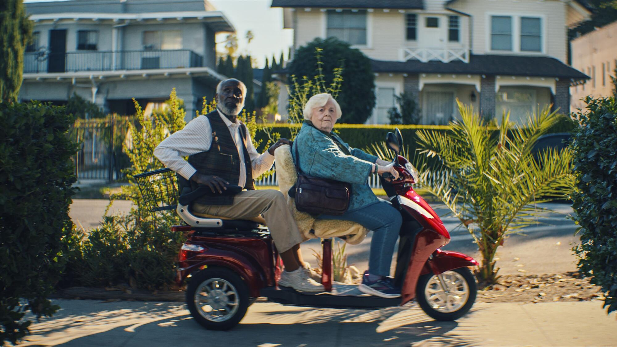 A man and a woman ride a mobility scooter.