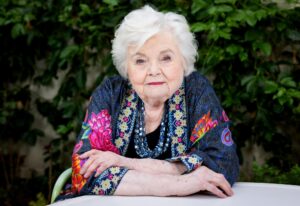 June Squibb sits outdoors, arms resting on a table, for a portrait.