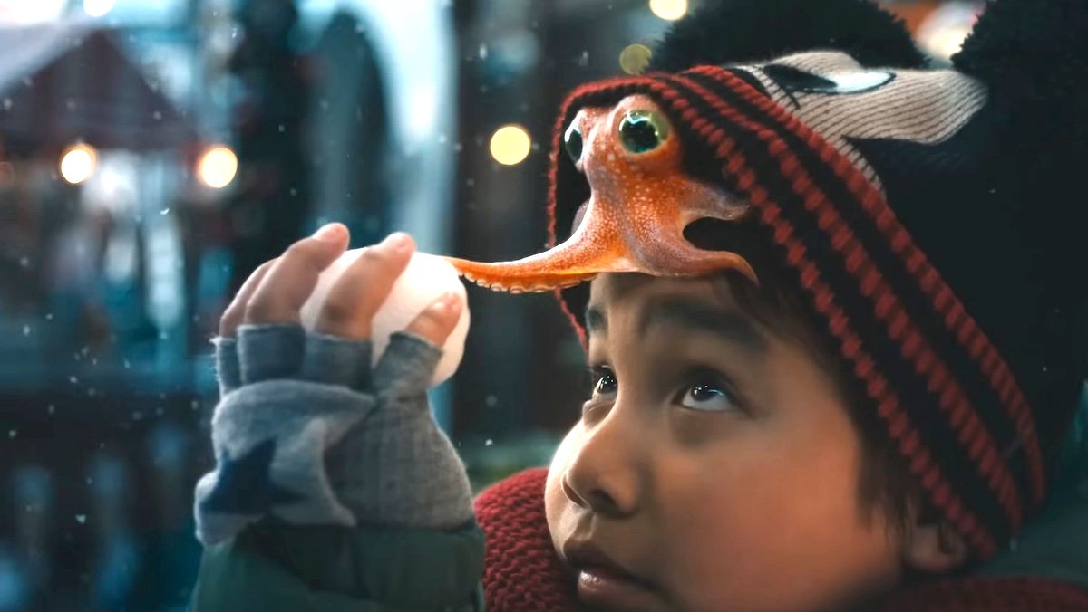 An orange octopus underneath a Mickey Mouse winter hat reaches out for the snowball held by the young boy whose head he's on from Disney's new Holiday short, the boy and the octopus