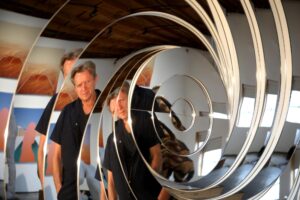 Artist Doug Aitken is reflected in the mirrored spirals of an artwork.