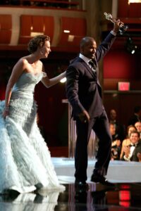 A man and woman in formal wear stand on the Oscars stage.