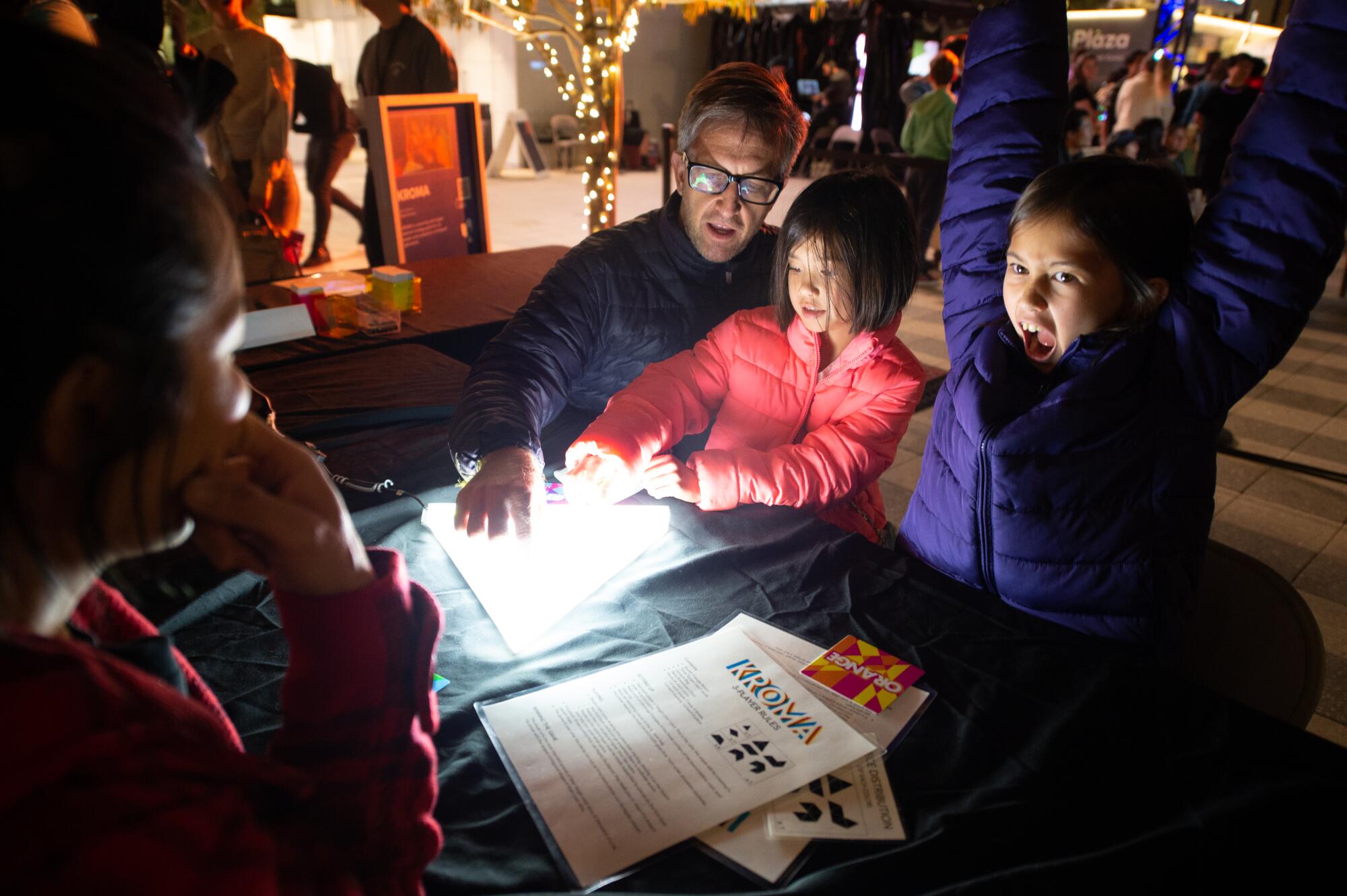 A group of young players celebrate around an illuminated triangle board game. 