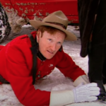 Conan O'Brien, dressed as a Canadian Mountie, lies in the snow caressing a woman's black boot.