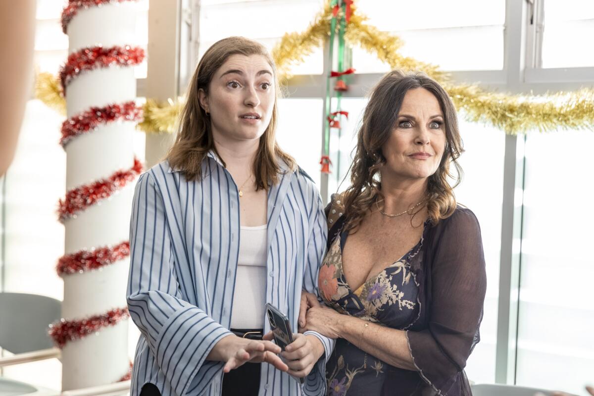 Two women stand near windows and a pole decorated in Christmas tinsel.