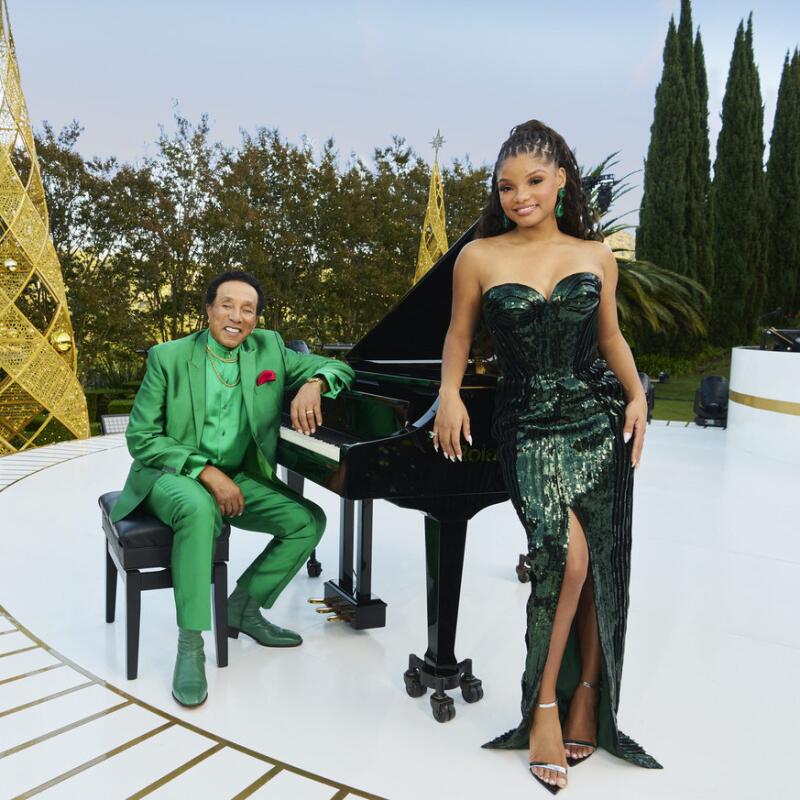 A man in a green suit sits on a bench, leaning on a piano, as does a woman standing in a green strapless gown.