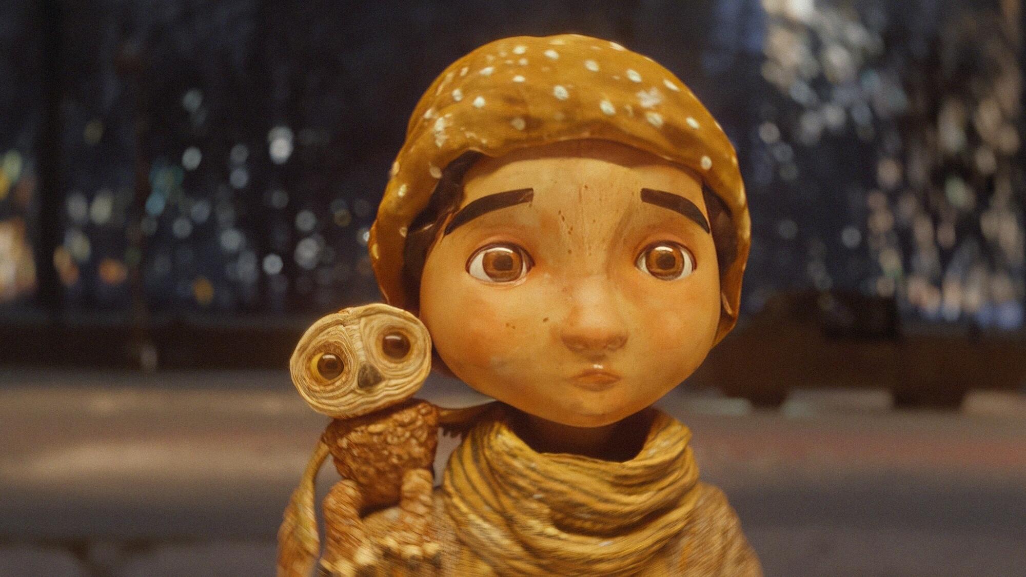 A little owl sits on the shoulder of a little girl wearing a hat and scarf.