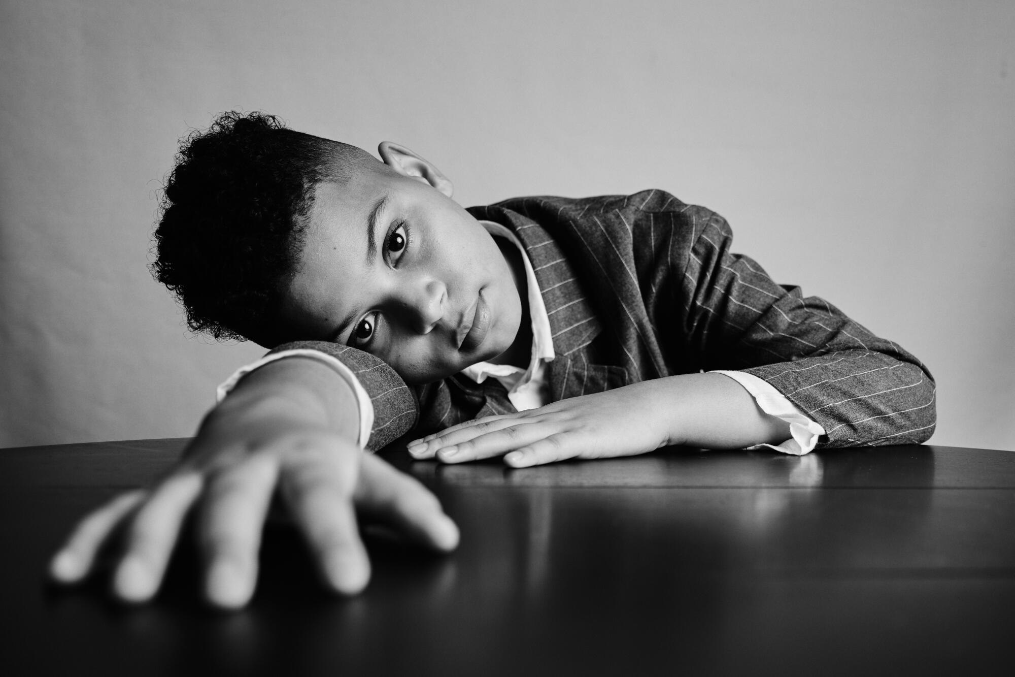 A young boy lays his head and arms flat on a table for a black-and-white portrait.