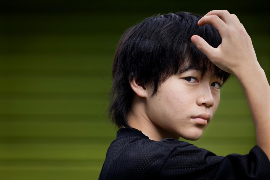 A teen boy puts his hand to his head for a portrait.