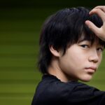 A teen boy puts his hand to his head for a portrait.