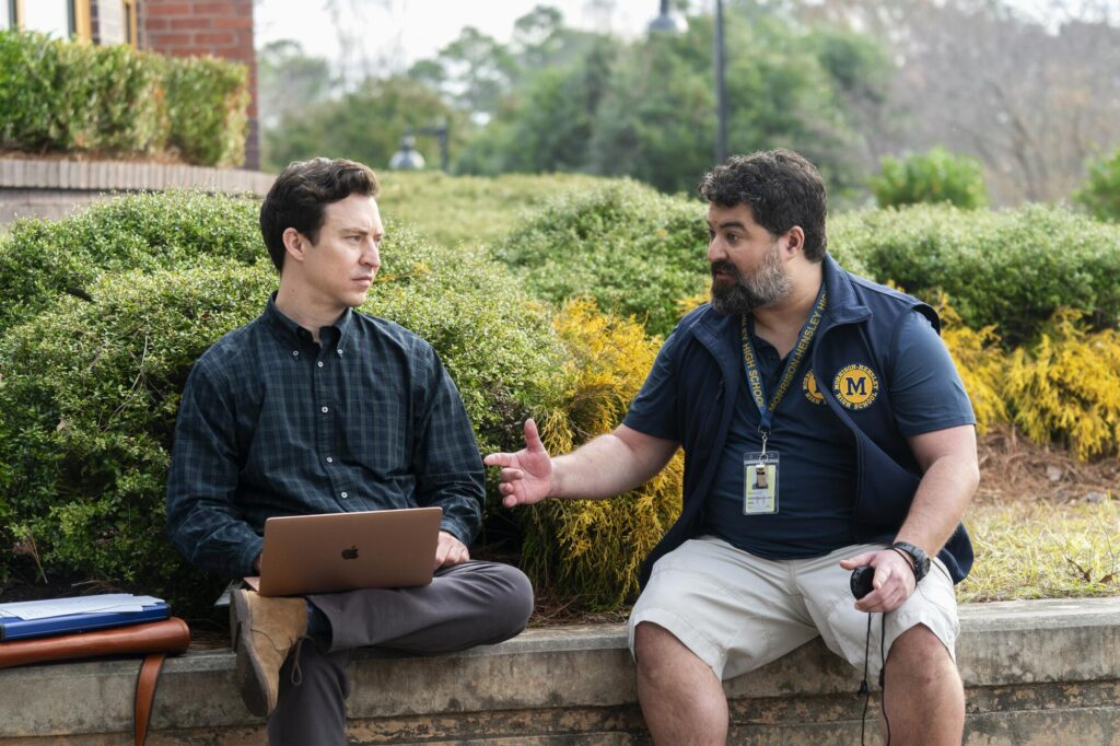 Two men sit on a cement wall and talk in a scene from "English Teacher."