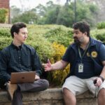 Two men sit on a cement wall and talk in a scene from "English Teacher."