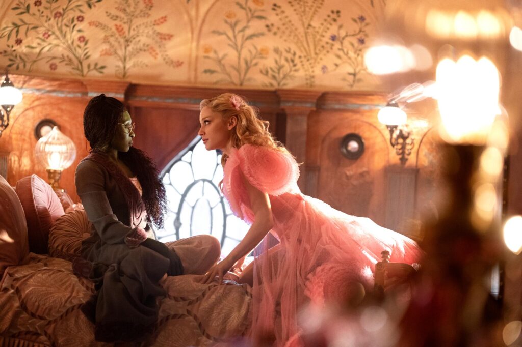 Cynthia Erivo and Ariana Grande sit on a bed in "Wicked."