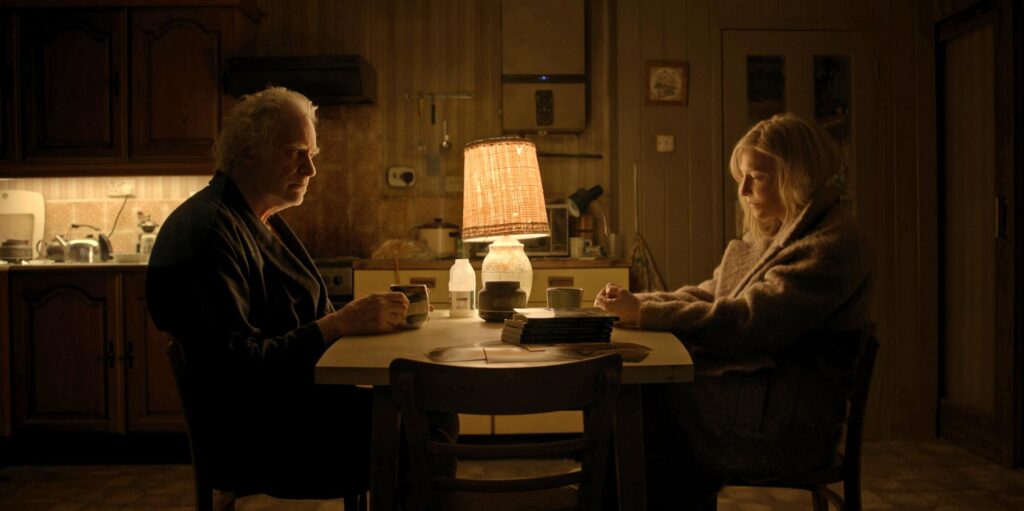 A man and woman sit at a dimly lit table looking serious in "Disclaimer."