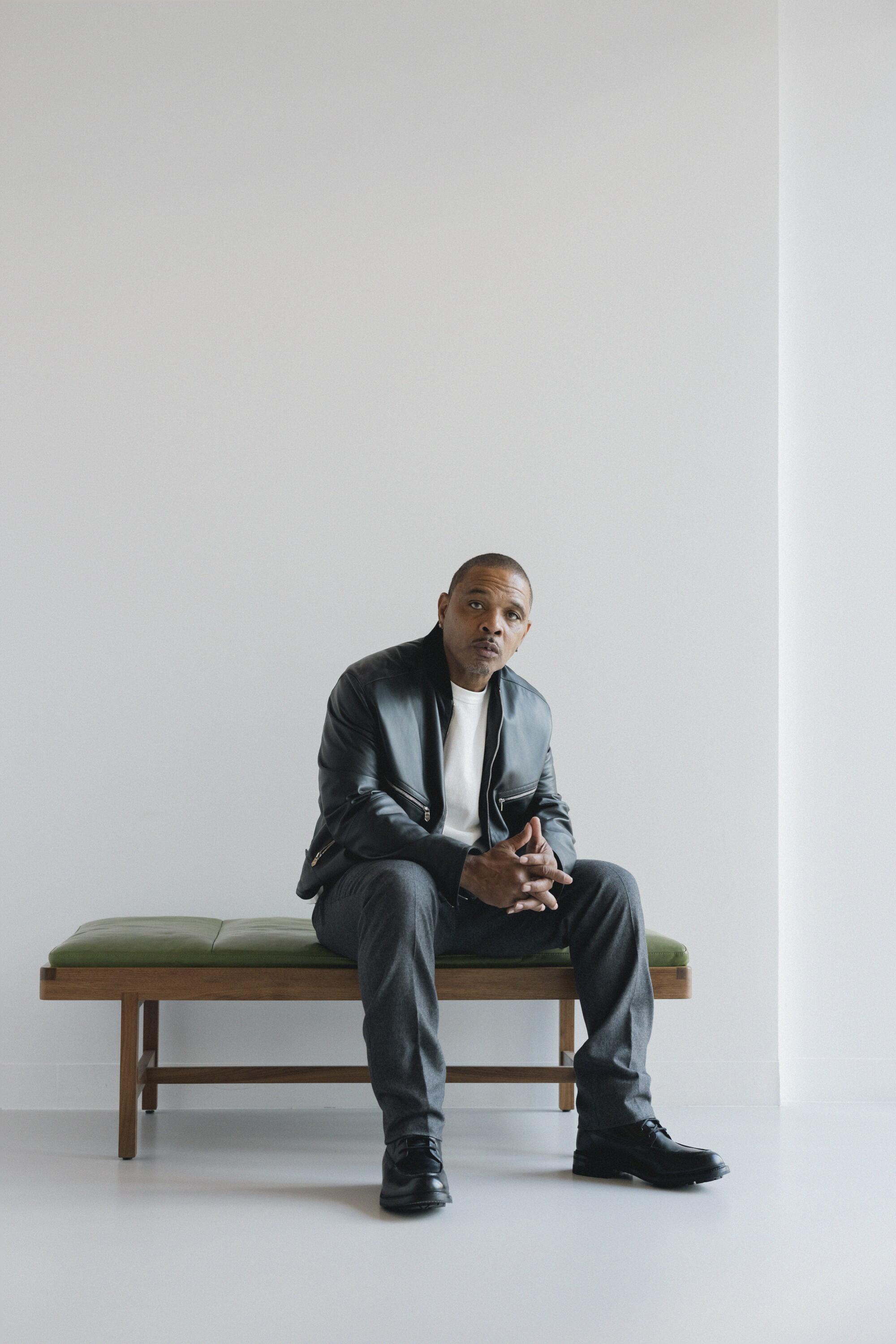 Clarence Maclin sits on a padded bench in front of a simple white wall for a portrait.