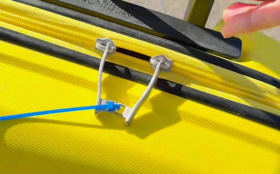 closeup of a bright yellow suitcase with zip ties on the zippers