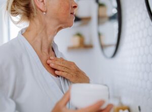 A woman applies moisturizer to her decolletage area