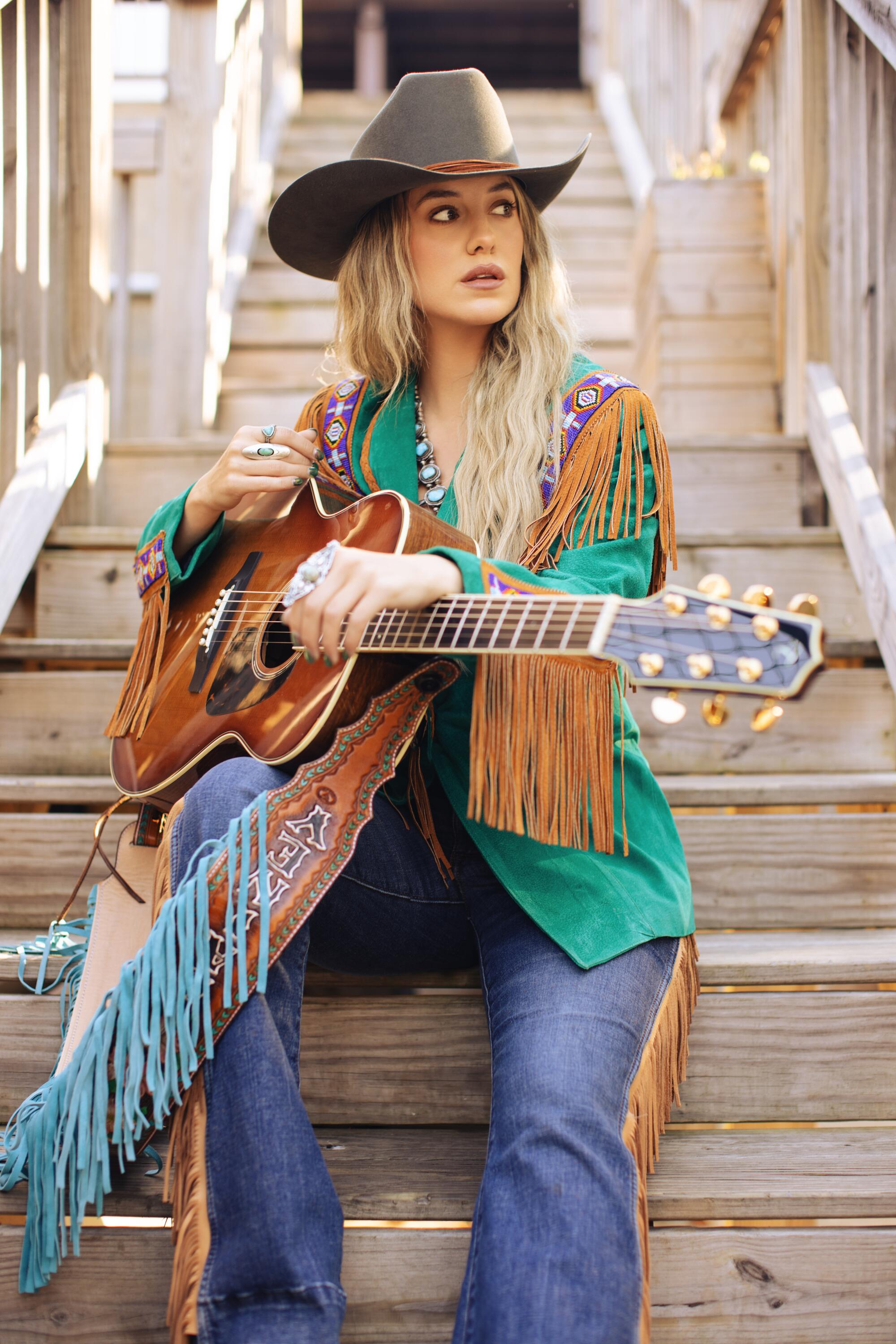 Country singer Lainey Wilson sitting on stairs with guitar.