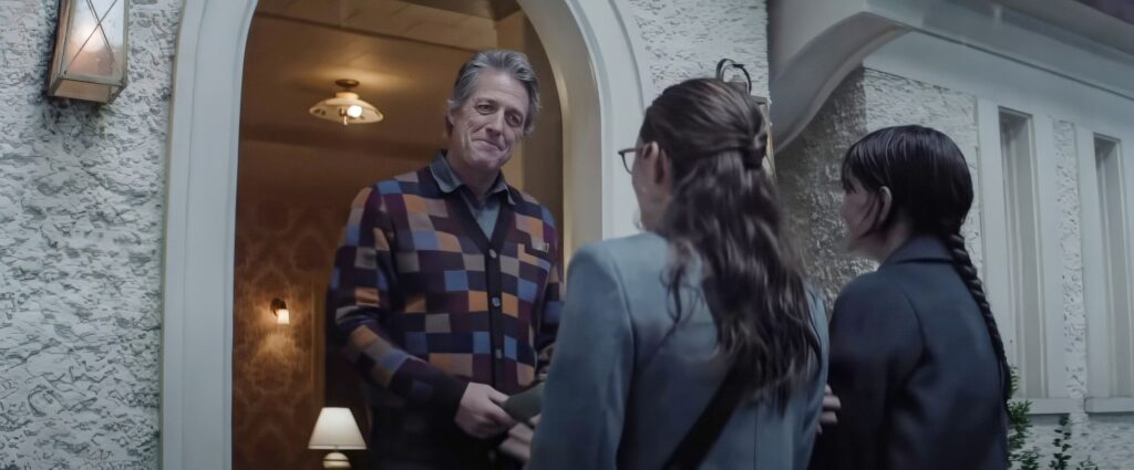 Mr. Reed (Hugh Grant, wearing a broad smile and a busy, patterned sweater-vest) greets a pair of Mormon missionaries (Sophie Thatcher and Chloe East) at the door of his house in Heretic