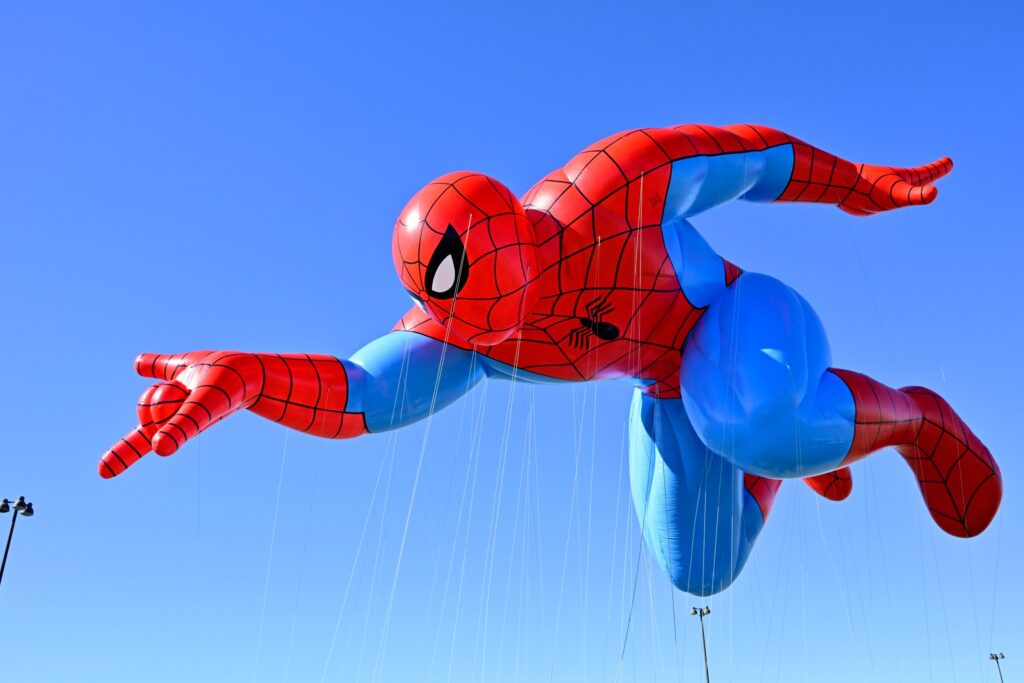 The Spider-Man parade balloon flies over Macy’s Balloonfest Preview. He’s depicted mid-webswing, with one hand extended, and has notably muscular thighs based on the art of John Romita Sr.