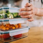 Close-up shot of female hands holding glass containers with fresh raw vegetables.