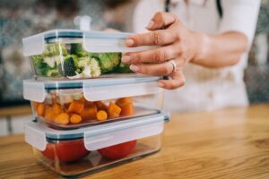 Close-up shot of female hands holding glass containers with fresh raw vegetables.