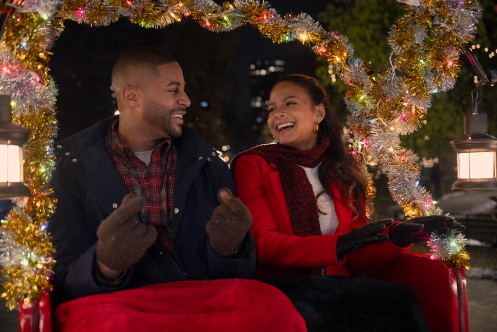 A man and a woman smiling while sitting in the back of a christmas-themed carriage in Meet Me Next Christmas.