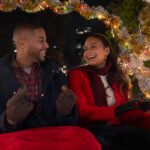 A man and a woman smiling while sitting in the back of a christmas-themed carriage in Meet Me Next Christmas.