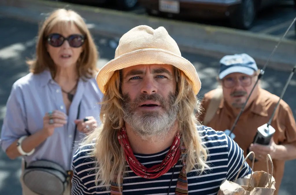 A bearded Chris Pine wearing a pale beach hat in front of Annette Bening and Danny DeVito in Poolman.