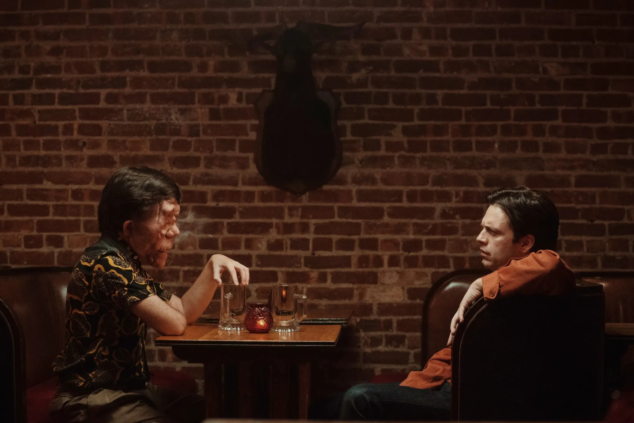 Adam Pearson and Sebastian Stan seated across from one another at a booth in a restaurant in A Different Man.