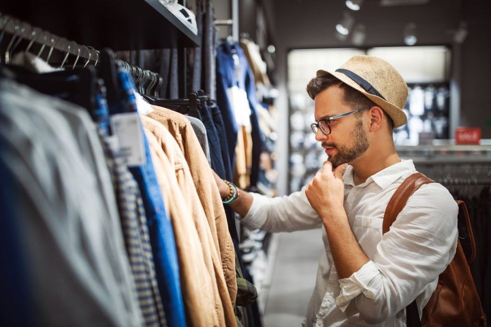 A young man in a hat and glasses shops for clothes in a store