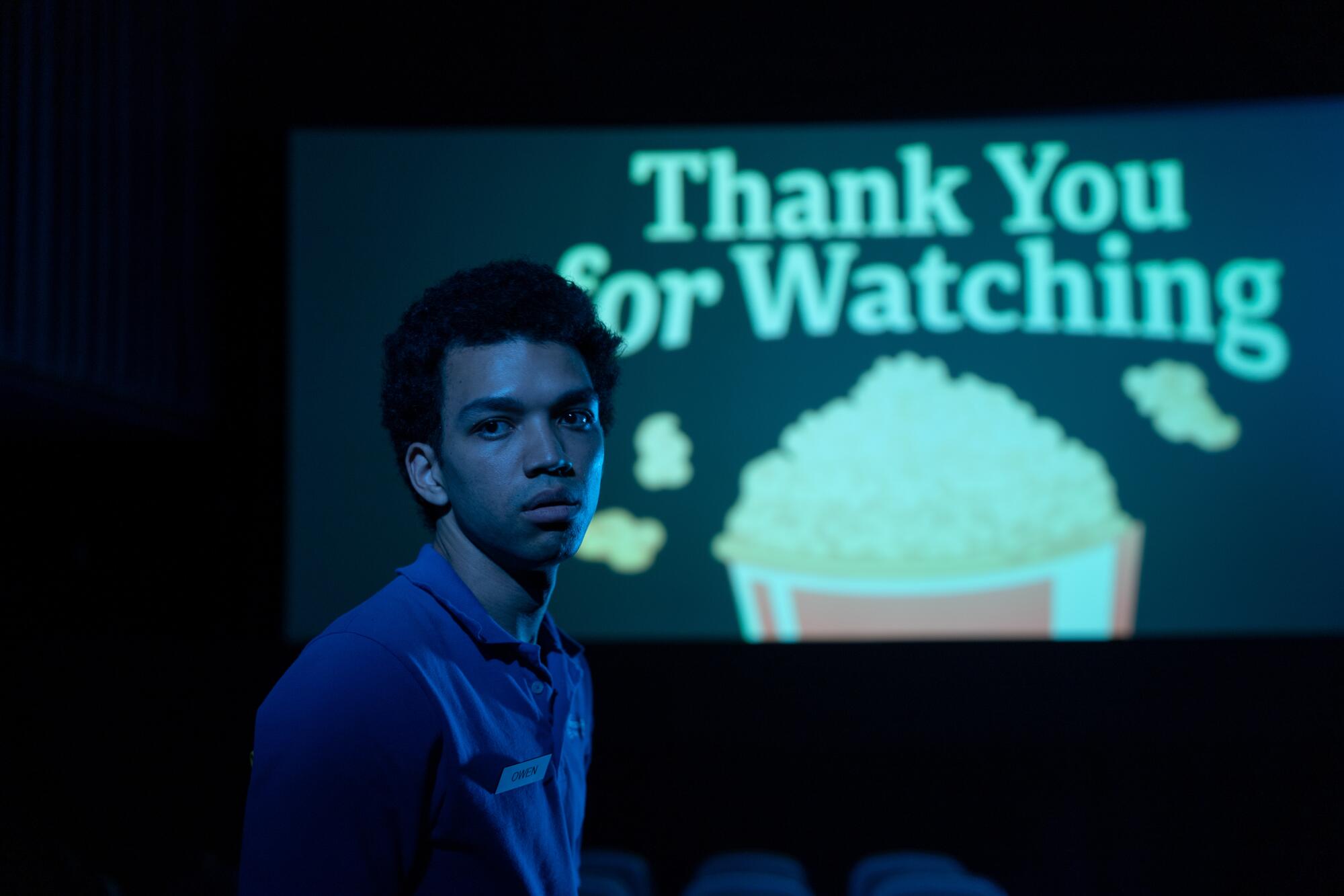 A young man stands with a lighted screen showing a bucket of popcorn behind him in "I Saw the TV Glow."