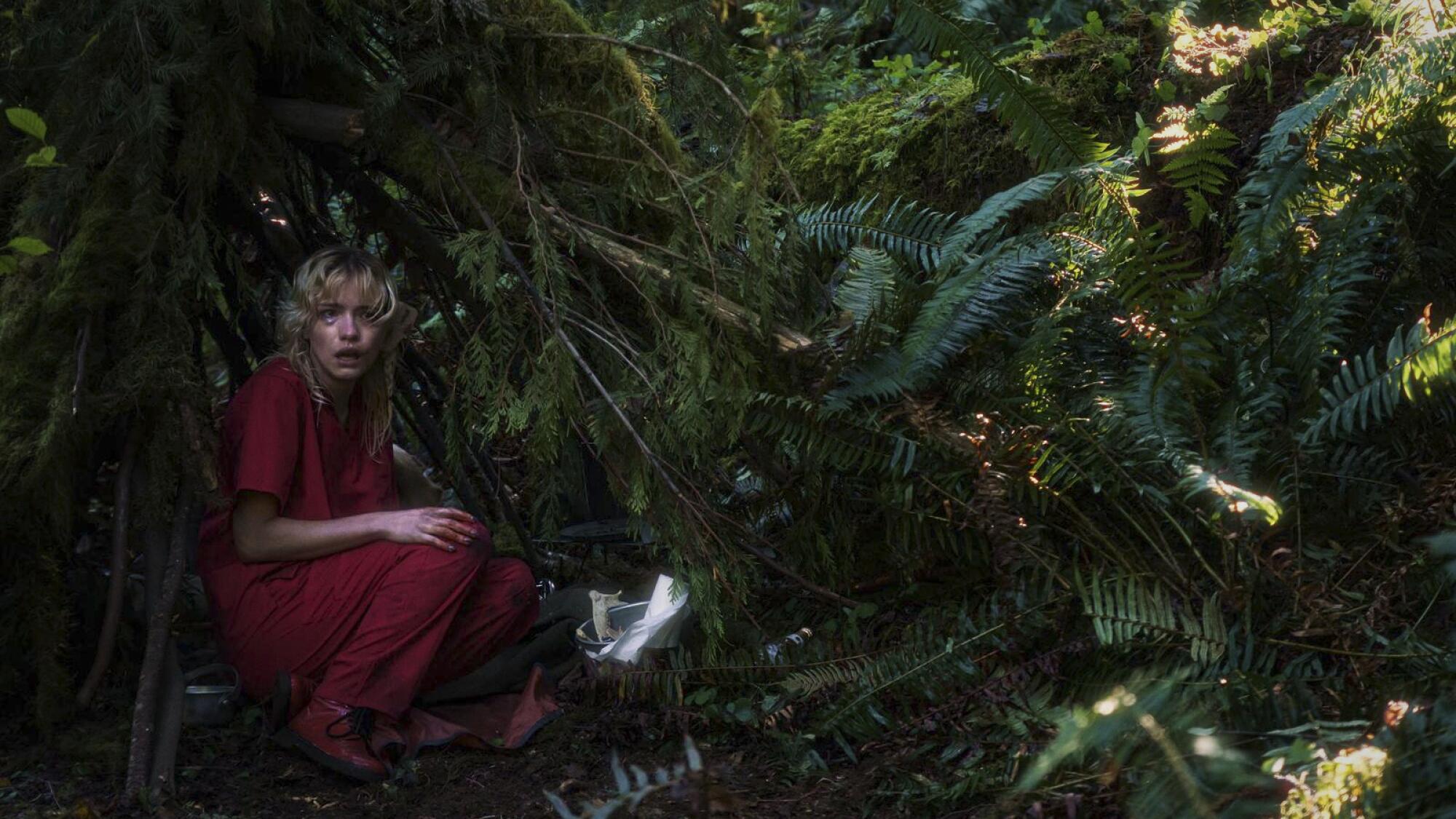 A scared-looking woman crouches beneath branches in a forest in "Strange Darling."