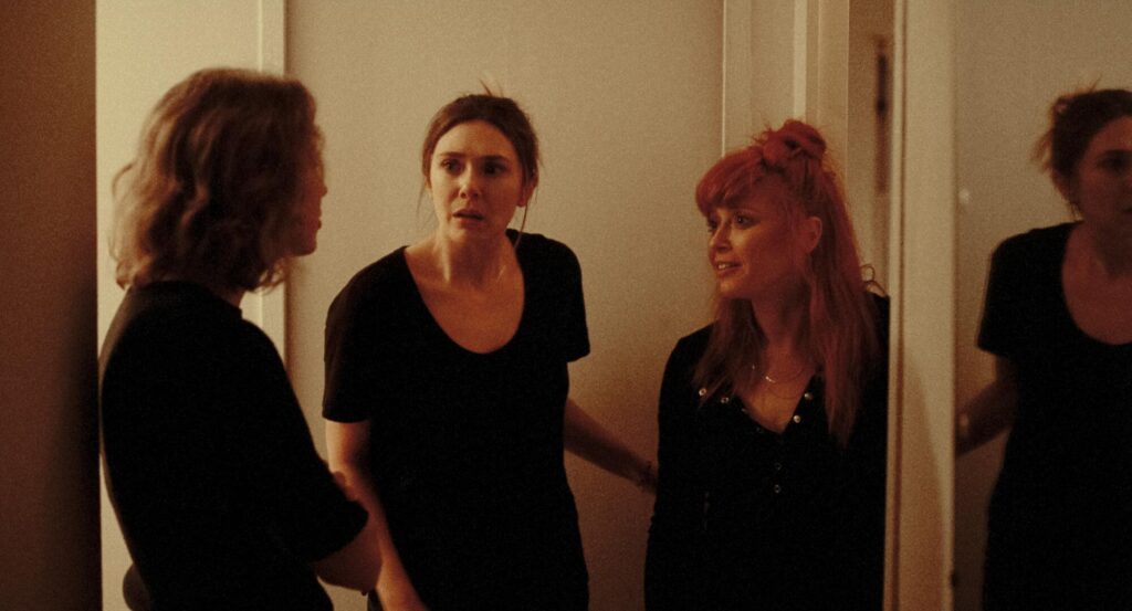 Three women talk in a hallway in a scene from "His Three Daughters."