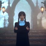 Jenna Ortega as Wednesday Addams with her arms crossed in front of stairs leading to an archway