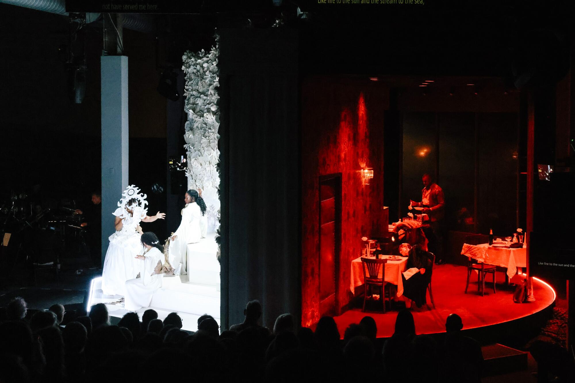 A revolving circular stage has singers costumed in bright white on one side, performers bathed in red light on the other. 