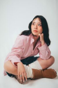 Echo Wu sitting cross-legged while dressed in a striped shirt, shorts and boots